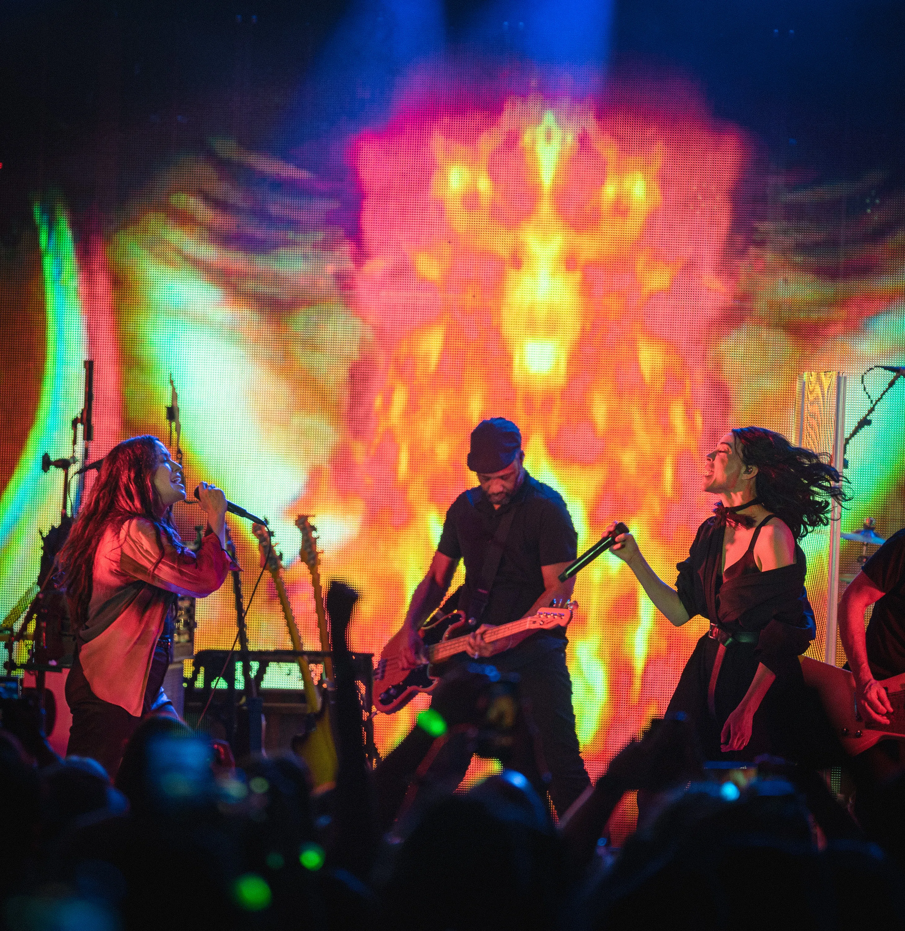 Alanis Morissette and St. Vincent singing toward one another with a musician between them
