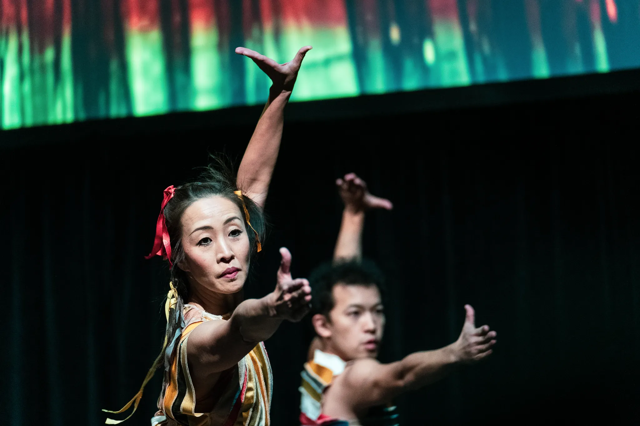 A dancer extending one hand forward and raising the other, echoed by a dancer behind her
