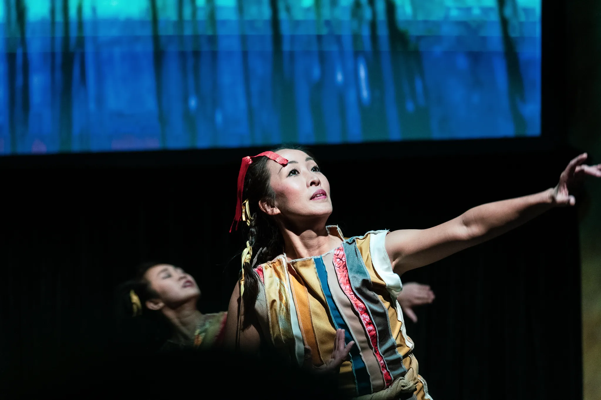 A dancer reaching outward beneath blue stage projections