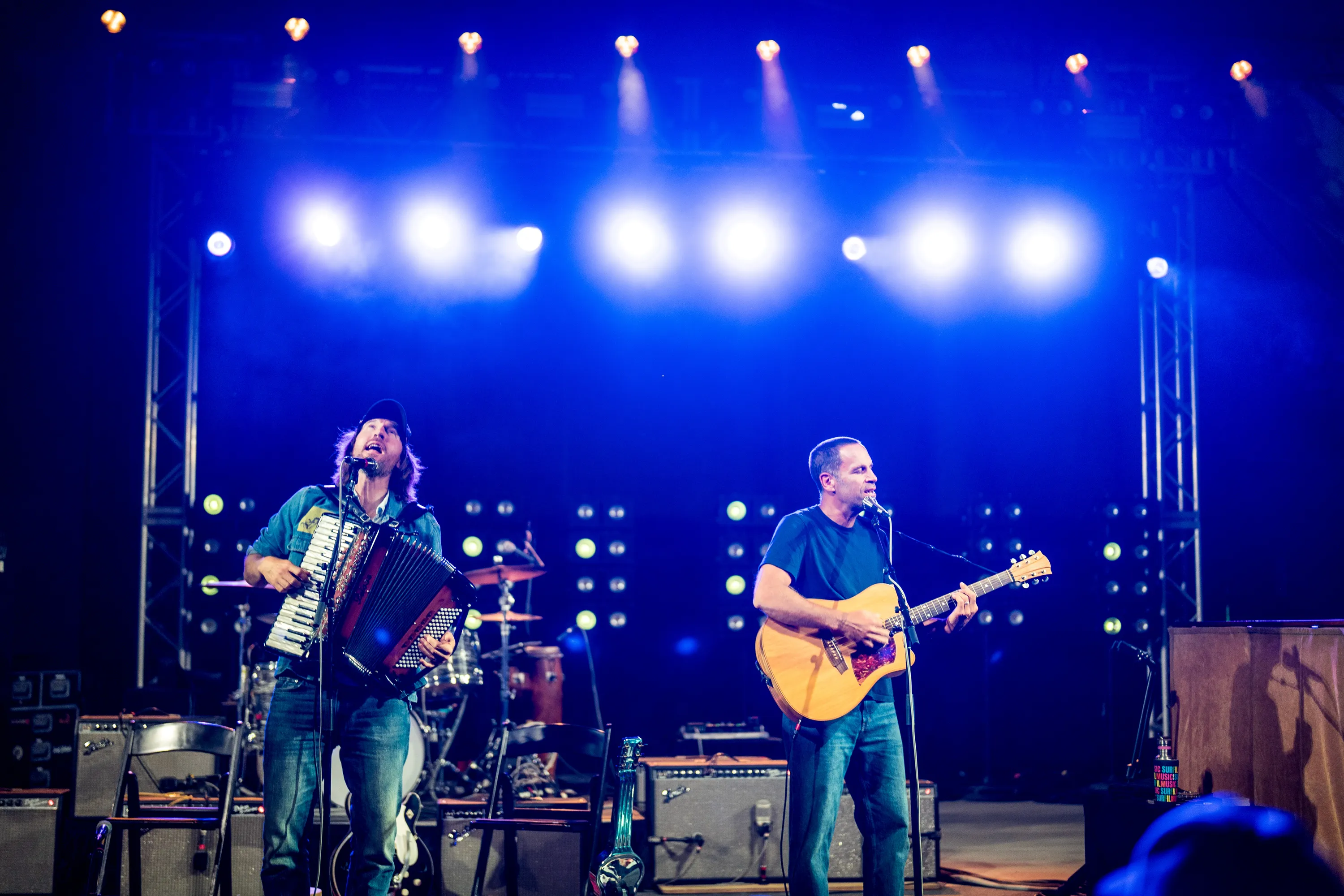 Jack Johnson singing and playing guitar beside an accordion player under blue stage lights
