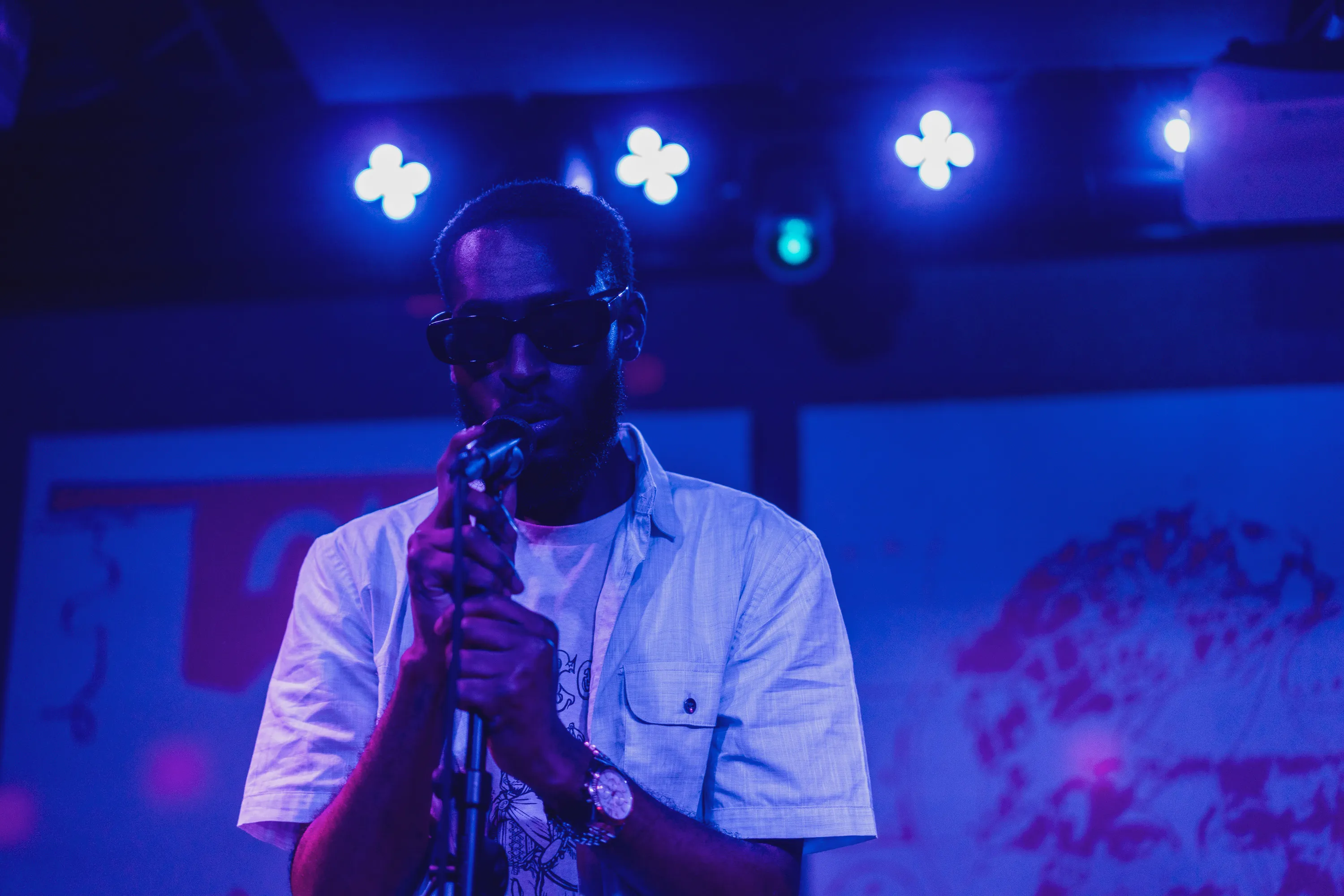 A vocalist in sunglasses holding a microphone under blue stage lights