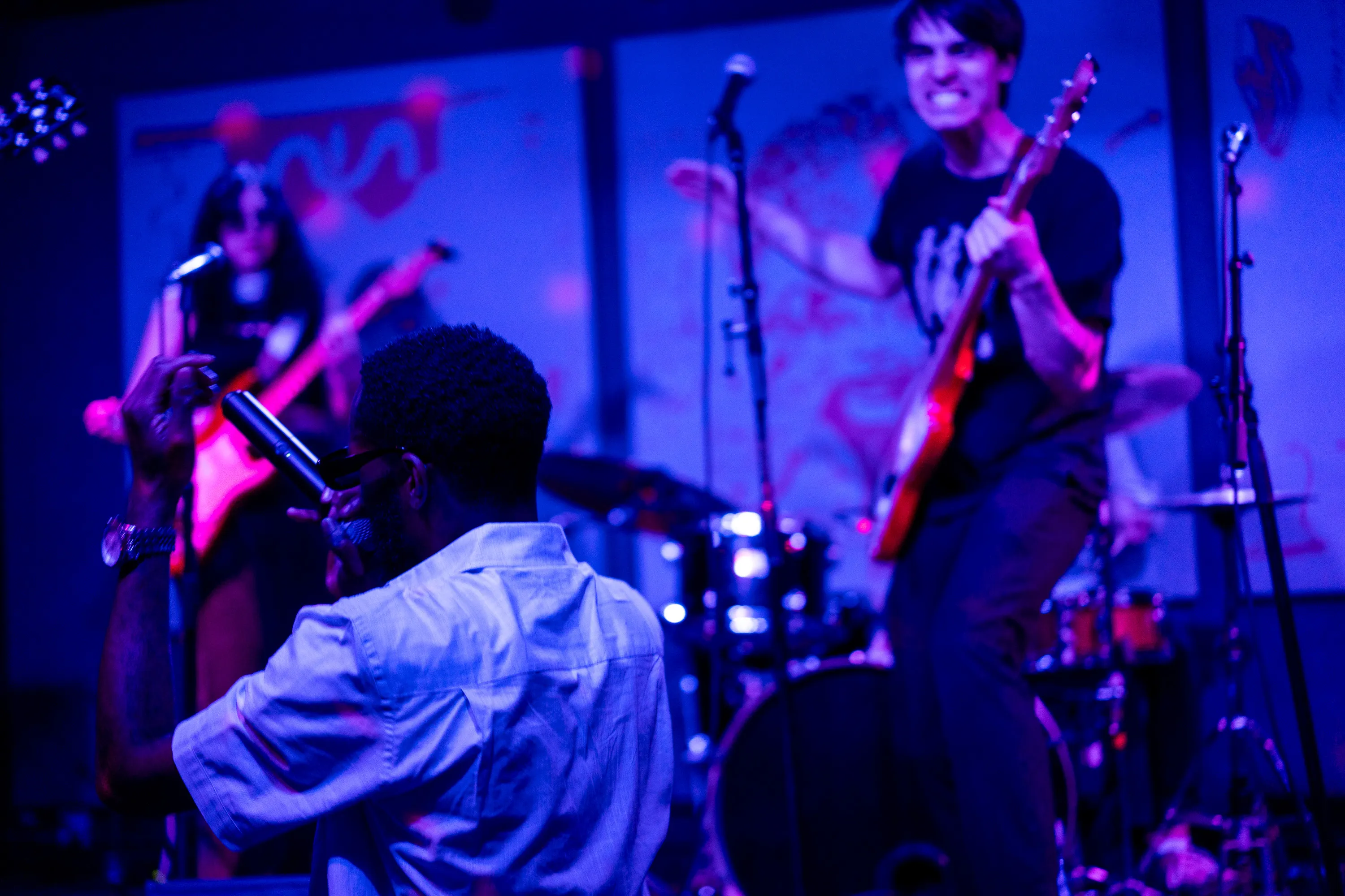 A vocalist turning toward the band as a guitarist plays
