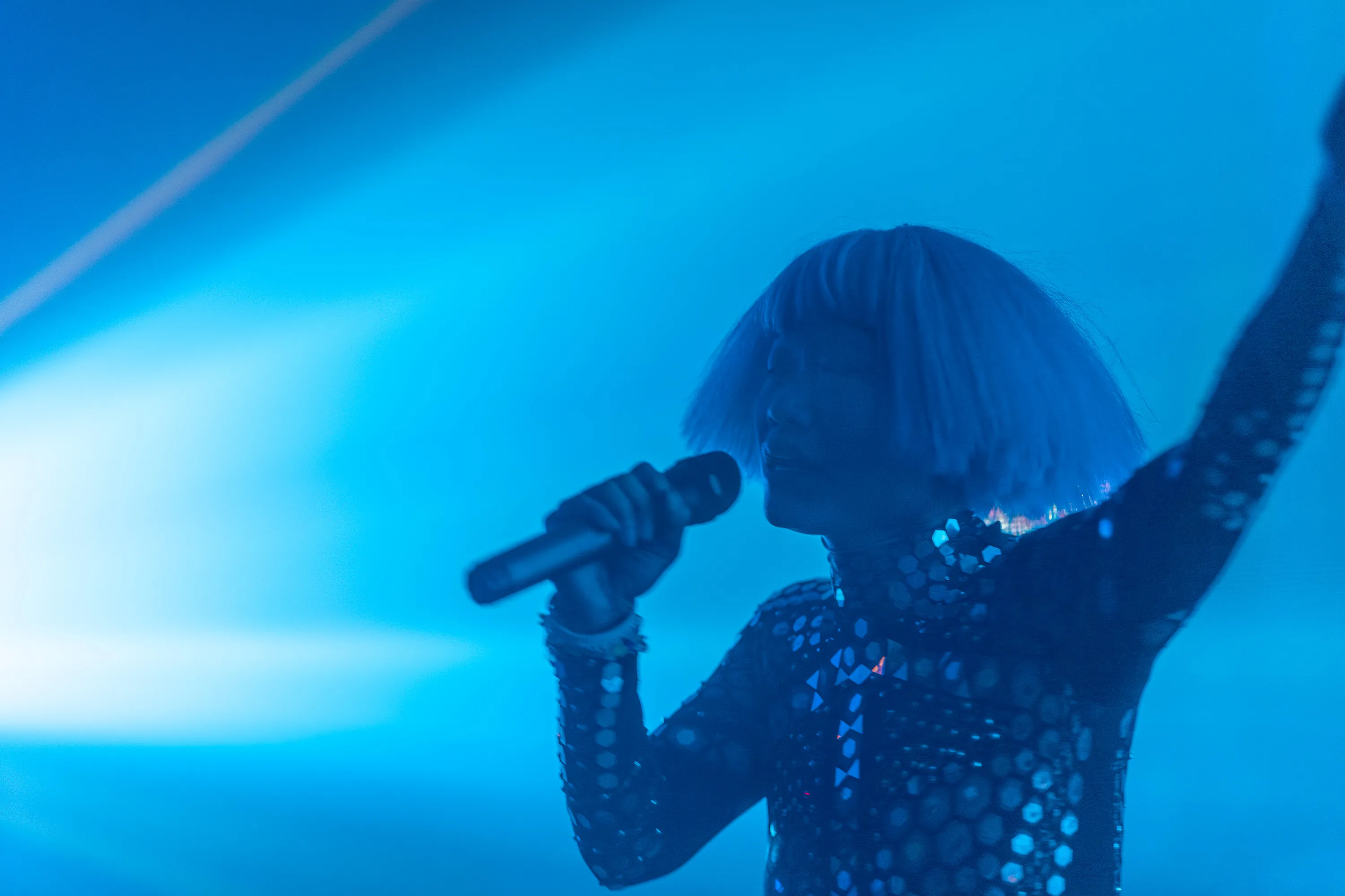 Olive silhouetted in blue light, singing with one arm raised